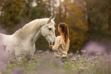 Genç bir kadın, sonbaharda açık havada yabani bir çiçek tarlasında beyaz İspanyol boynuzuyla sarılıp etkileşime geçiyor.