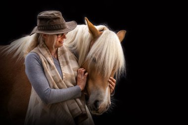 A woman cuddles with her haflinger horse in front of black background clipart