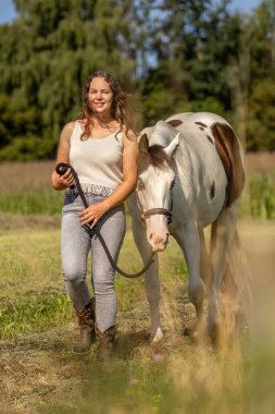 Gülümseyen genç bir kadın yaz doğasında bir boya atıyla bağ kuruyor.