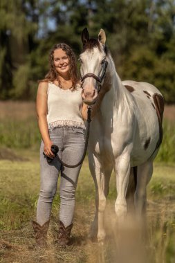 Gülümseyen genç bir kadın yaz doğasında bir boya atıyla bağ kuruyor.