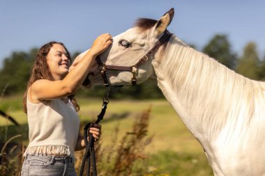Gülümseyen genç bir kadın yaz doğasında bir boya atıyla bağ kuruyor.