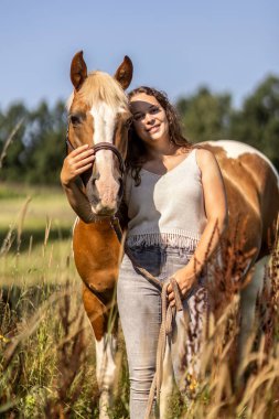 Haflinger 'la bağ kuran genç bir kadın yazın dışarıda Pinto mare' i karşılıyor.
