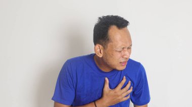  Tişört giymiş, terden sırılsıklam olmuş Asyalı bir adam kalp krizinden dolayı göğüs ağrısına göğüs ağrısına göğüs ağrısı çeken, göğüs ağrısı çeken bir adamın fotografik görüntüsüne dayanır.              