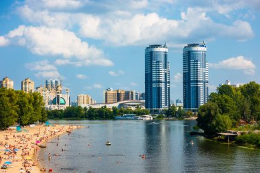 Kyiv 'deki hidropark. İnsanlar sahilde nehrin yanında dinleniyor. Uzakta ikiz kulelerin bina.