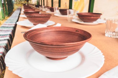 Açık hava yemek alanında uzun bir masada kil tabaklar..