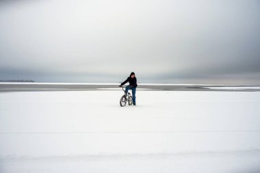 Gençler kışın karlı bir alanda bisiklet sürerler..