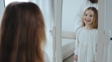 Genç anne ve 6 yaşındaki tatlı kız sabahları evde birlikte vakit geçiriyorlar. Anne küçük kızını aynanın önünde tarıyor, 4K video.