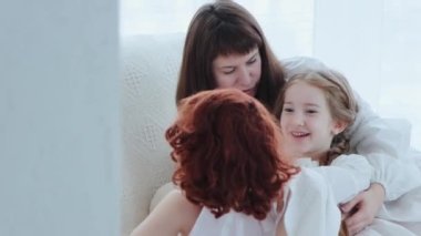 Mutlu bir ailenin portresi. Genç anne ve küçük kızı bir kanepede oturup evde eğleniyorlar, 4K orta çekim görüntüleri.
