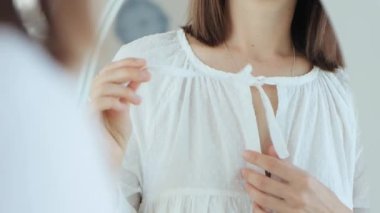 Genç bir kadının yakın plan fotoğrafları, aynanın önünde eski moda beyaz bir pijama dantelini çözer, 4K video..