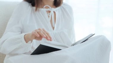 Eski moda pijamalı güzel esmer kadının portresi bir kitap okuyor ve kanepede otururken çay ya da kahve içiyor.