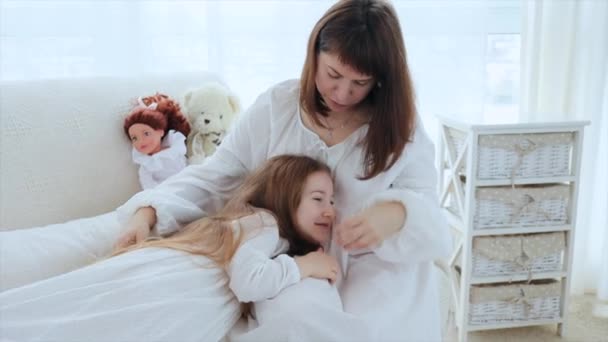 幼い大人の母親は幼い娘とソファに座り 甘い会話を交わしている ママは娘を頭の上にパス — ストック動画