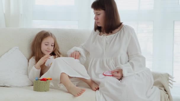 若いです大人の母親と小さな娘の服を着て昔ながらの白いパジャマは ソファに座って刺繍フレームと一緒に刺繍 4Kビデオ — ストック動画