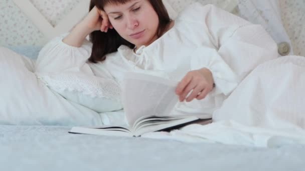 身穿白色复古式睡衣的年轻漂亮女人躺在床上 在卧室里看书 中间拍摄了4K段视频 — 图库视频影像