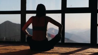 Genç bir kadının silüeti pencerenin yanında lotus pozisyonunda duruyor. Farkındalık, yoga ve meditasyon konsepti, 4k