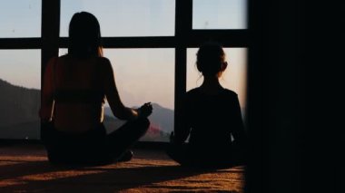 Anne ve kızının silueti birlikte meditasyon yapıyor. Lotus pozisyonunda otururlar pencereye dönük güzel dağ manzaralı.