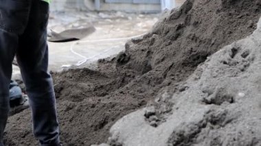 İnşaat alanında kumu vinç platformuna küreklerle yükleyen iki inşaat işçisinin yakın çekimi, 4K.