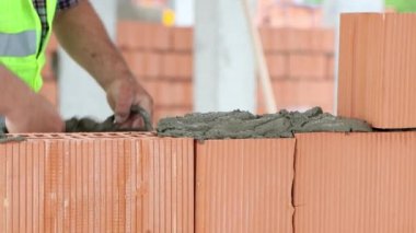İnşaatçı duvara beton harç uygular ve tuğla döker. İnşaat alanında tuğlalarla çalışıyor, 4K.