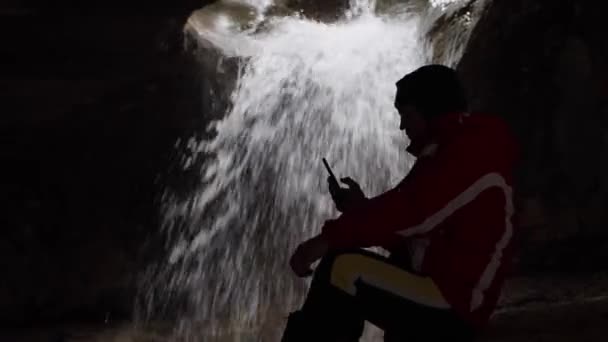 Yeraltı Şelaleli Mağarada Akıllı Telefon Kullanan Bir Adam Silueti Profil — Stok video