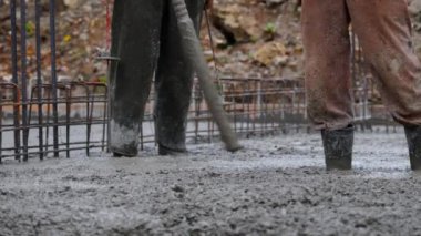 İnşaat alanı sahnesi. Plastik botlarla çimento döken işçiler temel atma sürecine aktif olarak katkıda bulunuyor..