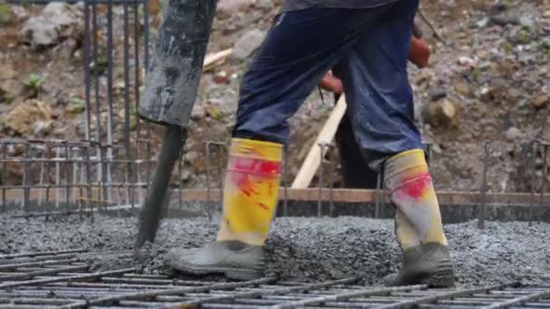 労働者は建設中の建物の基盤にパイプからコンクリートを運び 労働者の足を閉じます — ストック動画