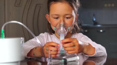 Evde zatürree tedavisi gören küçük bir kız çocuğu nebulizatörle nefes alıyor. Maske takıyor ve bu süreçte ilaçlarla oynuyor..