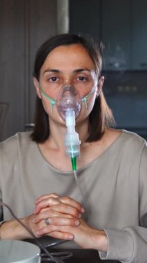Kadın, zatürree tedavisi sırasında maskeyle nefes alırken kameraya bakıyor. Dikey video.