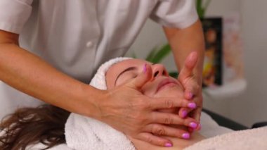 Tıbbi masaj salonundaki genç ve güzel bir kadın için terapötik yüz masajı tedavisi. Masaj terapisti bu sahnede felç hareketleri yapıyor..