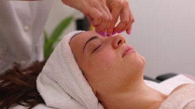Tıbbi masaj salonundaki genç ve güzel bir kadın için terapötik yüz masajı tedavisi. Masaj terapisti akupresyon tekniklerini gençleştirme ve yakın çekim için kullanıyor..
