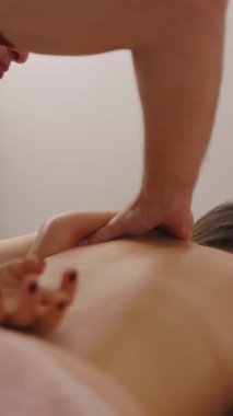 Masaj terapisti, genç bir kadına profesyonel bir sırt masajı yapıyor. Kürek kemiğinin derin dikkatine odaklanın. Okşama hareketleri, yakın çekim. Dikey video