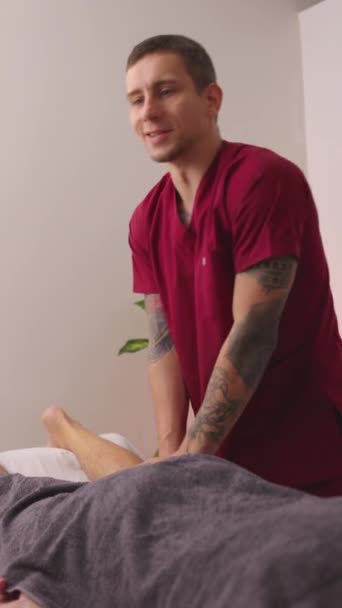 高圧の動きを持つ患者に治療脚マッサージを提供するプロの理学療法士 バーティカル映像 — ストック動画