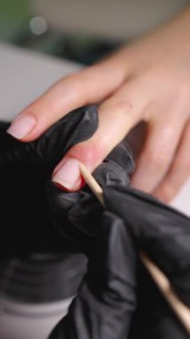 Tıbbi bir manikürcüye yakın plan: eldivenli manikürcü dişinin tırnağındaki tırnağı kaldırmak için satıcı kullanıyor. Dikey görüntüler.