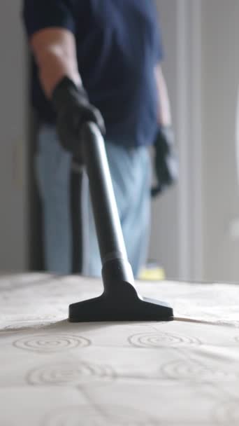 専門の掃除機が付いているマットレスを掃除する男 装飾された家具のクリーナー マットレスの真空の表面 バーティカルビデオ — ストック動画