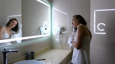Genç bayan uykusunda saçlarını oteldeki banyo aynasının önünde havluyla kurutuyor..