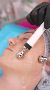 Kadın mikro akım tedavisi görüyor. Kozmetik uzmanından. Yakın çekim. Kozmetik prosedürleri yenileniyor. Donanım kozmetolojisi, dikey video biçimi.