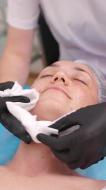 Güzellik uzmanı, yüzü peçeteyle soyan güzellik maskesini çıkarıyor. Güzellik kliniğinde müşteriler için estetik ameliyat. Cilt bakımı ve kozmetoloji spa konsepti. Dikey Video Biçimi.