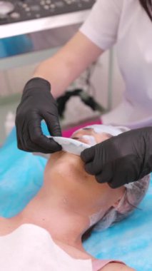 Kozmetikçi kadının yüzündeki sertleşmiş maskeyi çıkarıyor. Kozmetoloji, profesyonel bakım, spa tedavileri. Yüz maskesi. Dikey Video Biçimi.