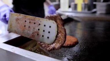 Fırında spatulayla sulu et köftelerini kızartıp ters çeviren bir şefin yakın çekimi. Hamburger hazırlama ya da restoran mutfağında yemek pişirme sahneleri için mükemmel..