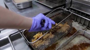 Bir aşçı kızgın yağdan kızarmış bir parça tavuğu maşa kullanarak alır, bu da onu bir tabağa peçeteyle koymadan önce fazlalık yağın damlamasına izin verir. Kızarmış tavuk ve yemek hazırlama..