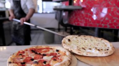 Aşçı adam tahta tahtaya sıcak pizza serer, fırıncının küreğinden çıkarır. Peynirli sıcak pizza, restoran yemeği..