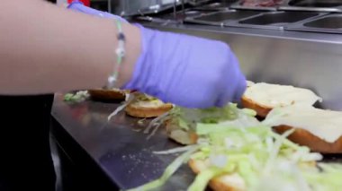 Fast food restoranındaki bir aşçı hamburgerleri toplarken lahana ve domates de dahil olmak üzere sebze koyar. Fast food hazırlama ve hamburger yapma sahneleri için mükemmel..