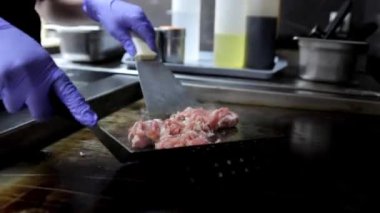 Bir restoran mutfağında, bir şefin elleri yakın planda kızartılmış et parçalarını spatula kullanarak fırında kızartırken gösterilir. Aşçılık tekniklerini ve pişirme sürecini vurgulamak için mükemmel.