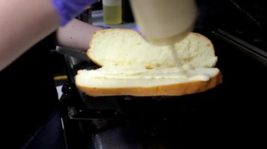 Eldivenli bir şefin elleri ekmeği sosla yağlar ve kızarması için fırına koyar. Sıradan bir yemek ortamında sandviç yapma sürecini sergilemek için ideal..
