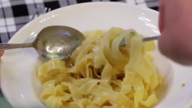Tabaktan çatalla spagetti çeviren ellerin yakın plan çekimi. Makarna ve İtalyan mutfağı zevki..