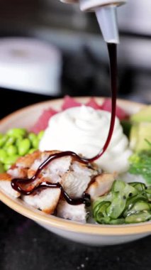 Hamur torbasından yakın plan sos ve peynir ve Japon dürüm kabında pilav, sebze, balık ve deniz yosunuyla serpiştirilmiş balzamik sirke. Dikey video biçimi