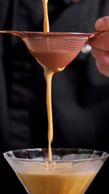 Bir barmen yakın çekimde eleğe doğru kokteyl sarıyor..