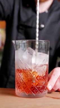 Bir barmen ağır çekimde kaşıkla alkollü bir içeceği buzla karıştırır. Dikey video formatında yakın çekim, kokteyl hazırlama ve içecek içeriği için mükemmel.