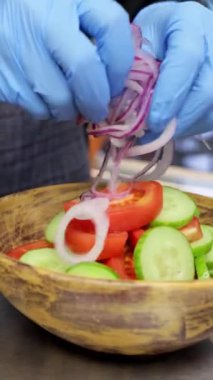 Şef salatalık, domates ve soğandan sebze salatası hazırlıyor. Tahta kasede salatanın yakın çekimi, dikey video..