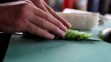 Suşi yaparken, şef bıçakla kesilmiş avokado biçer ve dikkatlice suşiye koyar. Sushi pişiriyorum, yakın plan..