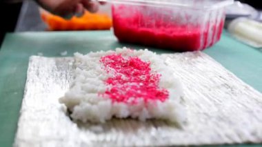 Yakın plan çekimde, Japon mutfağı suşi yaparken kırmızı balık havyarı suşi pilavı üzerine serilir..