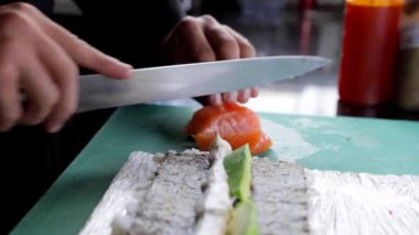 Bir şef, Philadelphia suşi sarması yapmak için somon balığını dilimliyor. Japon mutfağını ve suşi yapma tekniklerini yakın plan çekimde gösteriyor..